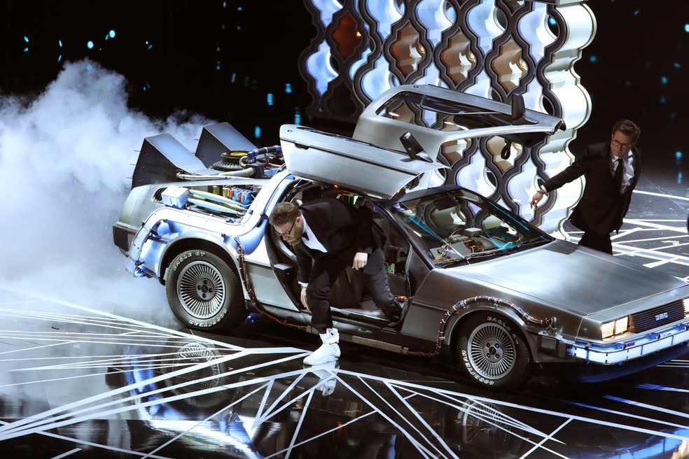 Seth Rogen e Michael J. Fox, o Marty McFly, de "De volta para o futuro", entram no palco com um DeLorean, a máquina do tempo do filme. — Foto: Lucy Nicholson / Reuters